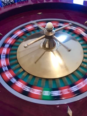 Une roue de roulette tournante avec une boule argentée en mouvement, montrant des cases numérotées rouges, noires et vertes floues dans un Soirée Casino animé.