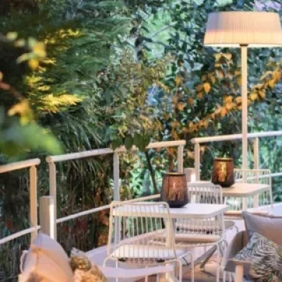 Espace extérieur avec chaises et tables en métal blanc, deux petites lanternes et une grande lampe - un endroit accueillant pour une soirée prestige dans la verdure tranquille du triangle d'or.